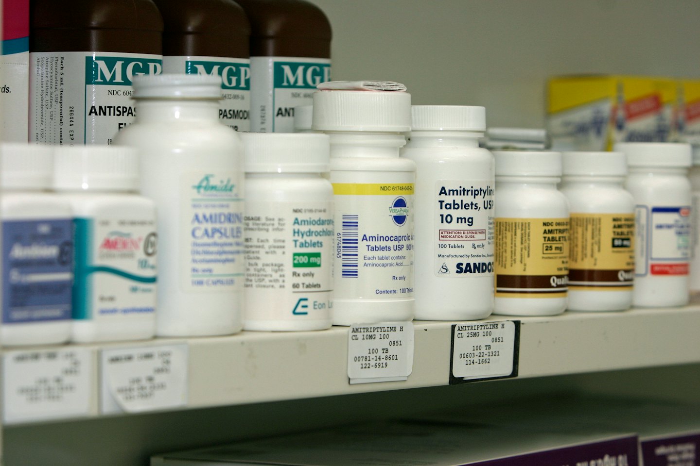 Medikamentenflaschen ordentlich auf einem weißen Apothekenregal.