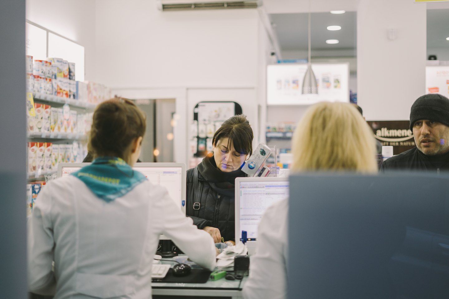 Kunden und Mitarbeiter interagieren an einem Apothekenschalter.