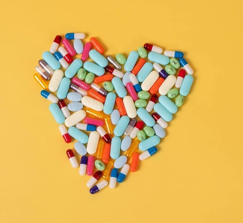 Colorful pills and capsules arranged in a heart shape.